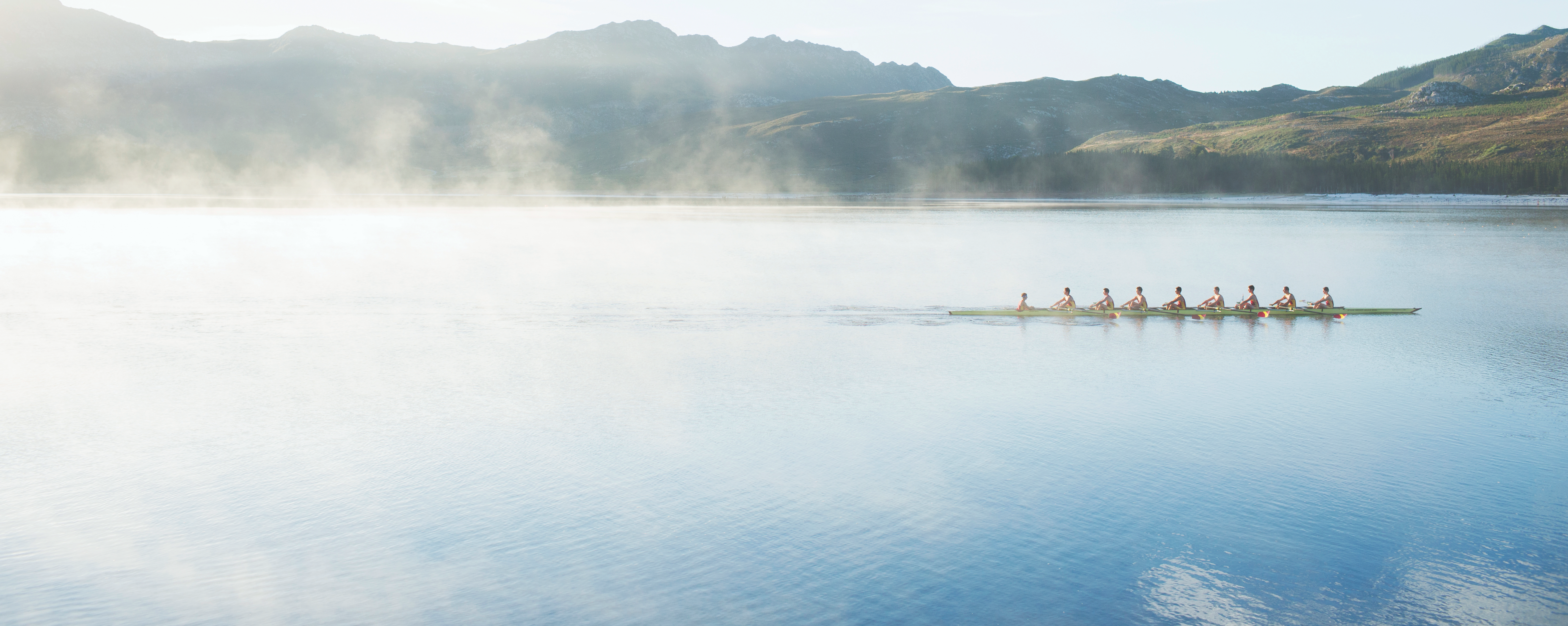Rowers on a misty lake with mountains in the background