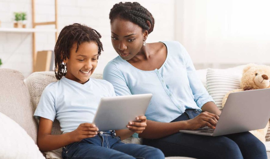 Woman and child sitting on a couch looking at a tablet. Woman as an open laptop on her lap.