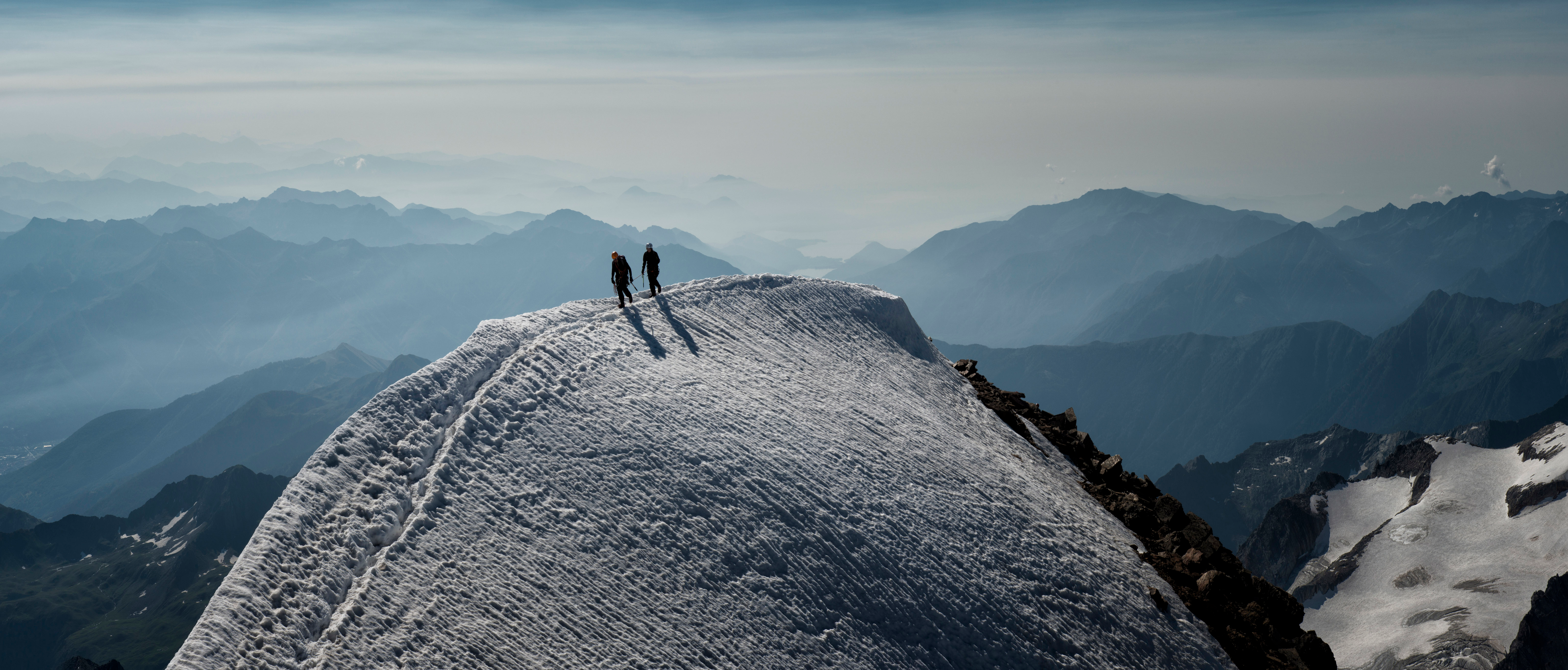 Two people at the crest of a snowy mountain