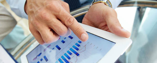 Close-up image of hands holding a tablet, pointing at the multiple graphs on the screen.
