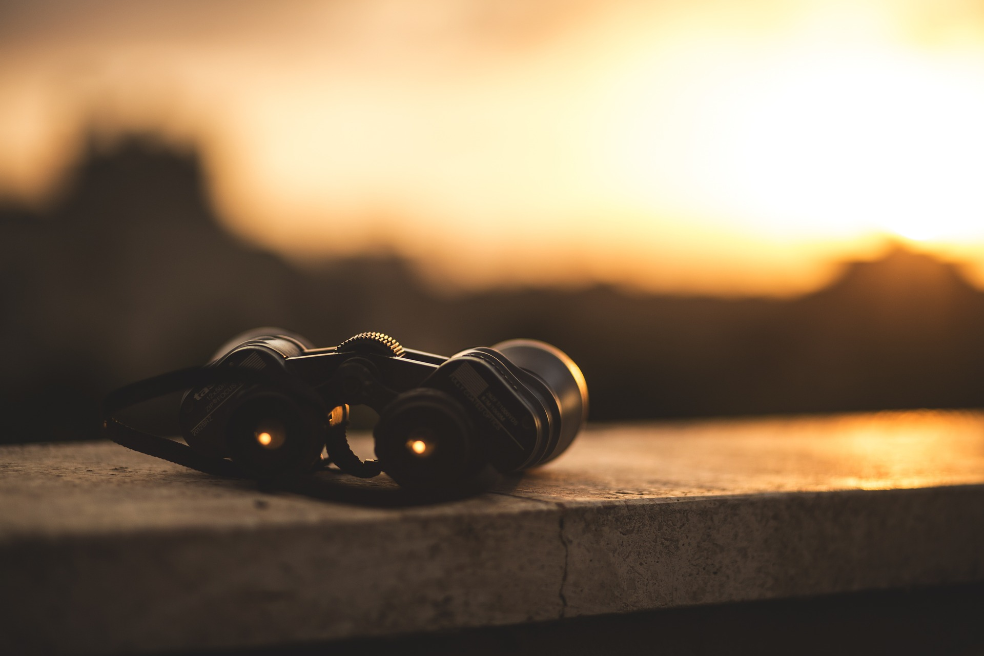 Binoculars on a ledge looking towards a sunset