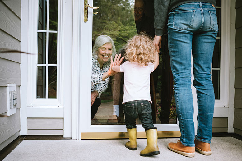 little-girl-visiting-grandparents-through-glass-door-in-page