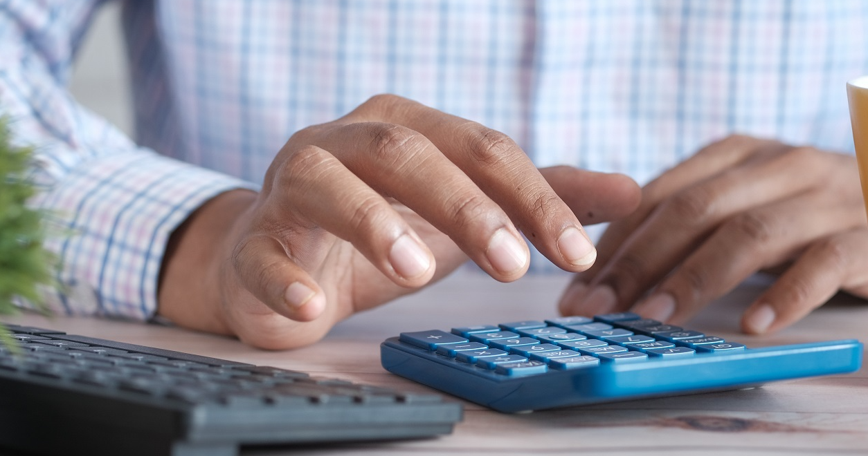 Close-up image of a person at a desk entering numbers on a calculator.