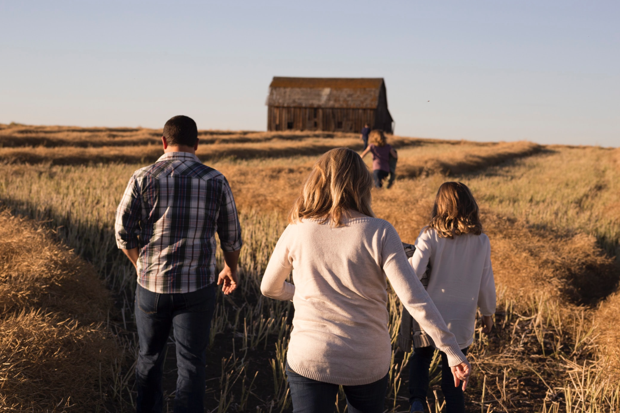 Family walking in a field towards a barn.