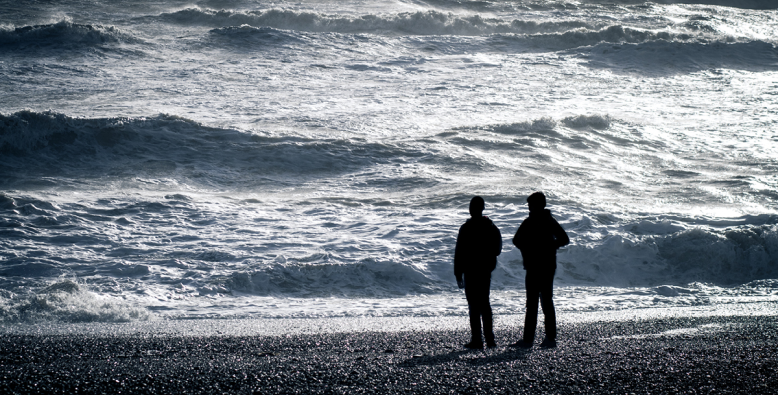 two people on beach looking at waves