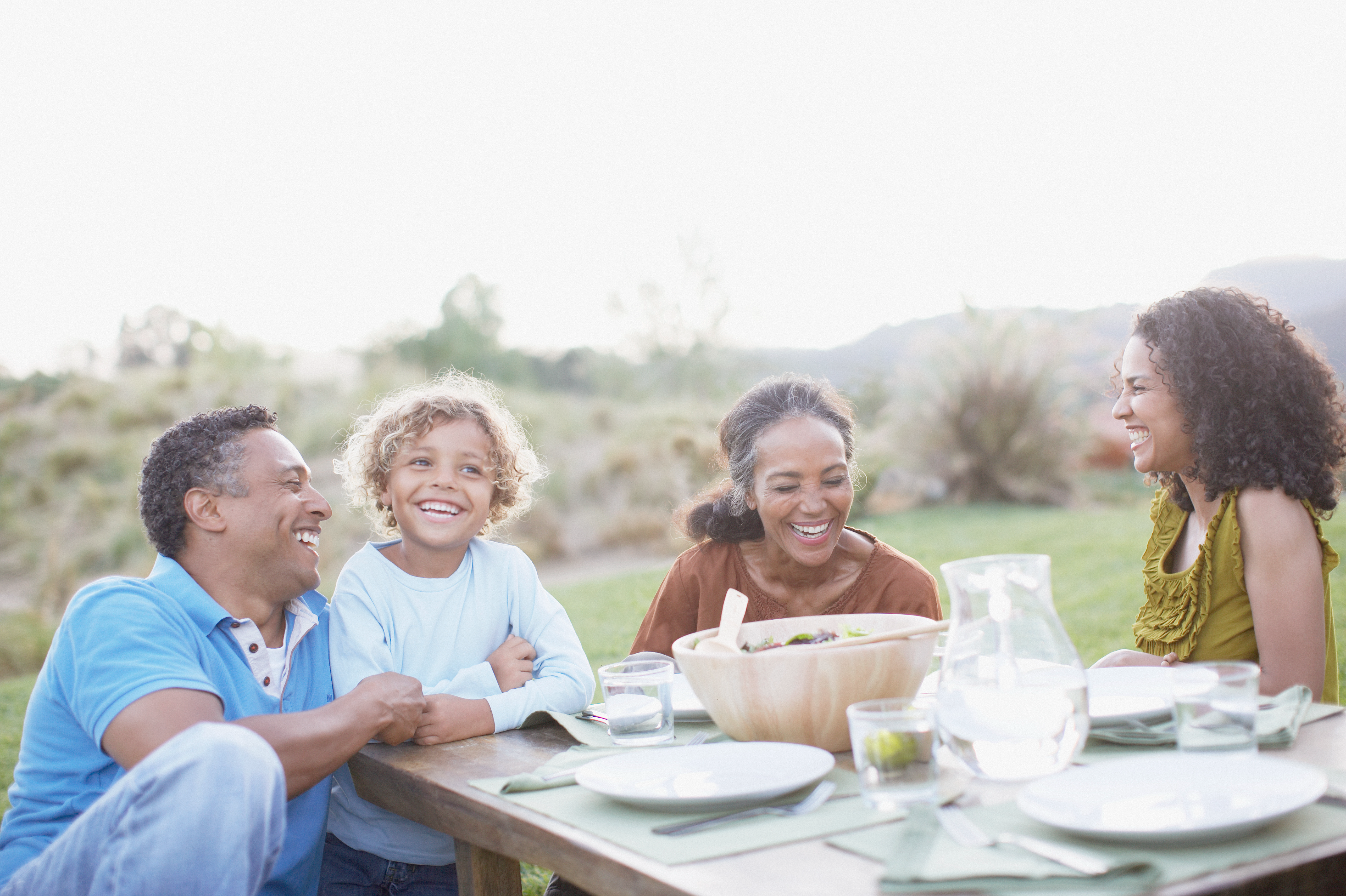 A family of four seated at a table, smiling and enjoying a meal outdoors