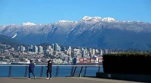 walkers along sea wall in Vancouver. Backdrop is city and mountains.