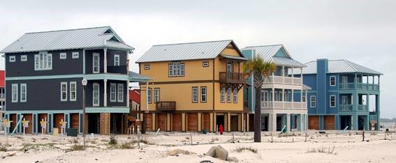 Four colourful raised beach houses facing a sandy beach