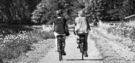 Two women riding bikes on a gravel path beside a lake. 