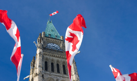Close up view of Parliament building tower with Canadian flags in the foreground. 