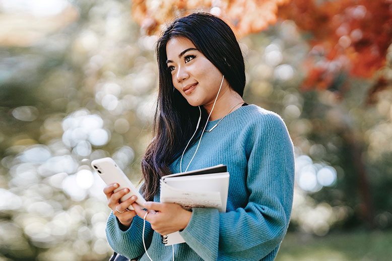 Young woman holding a notebook and listening to music on her mobile device