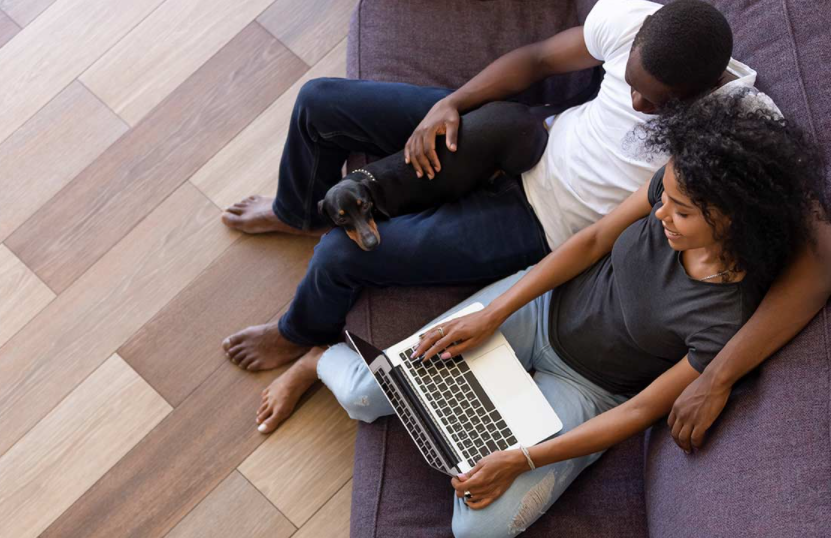 Couple sitting on a couch with a dog and a laptop