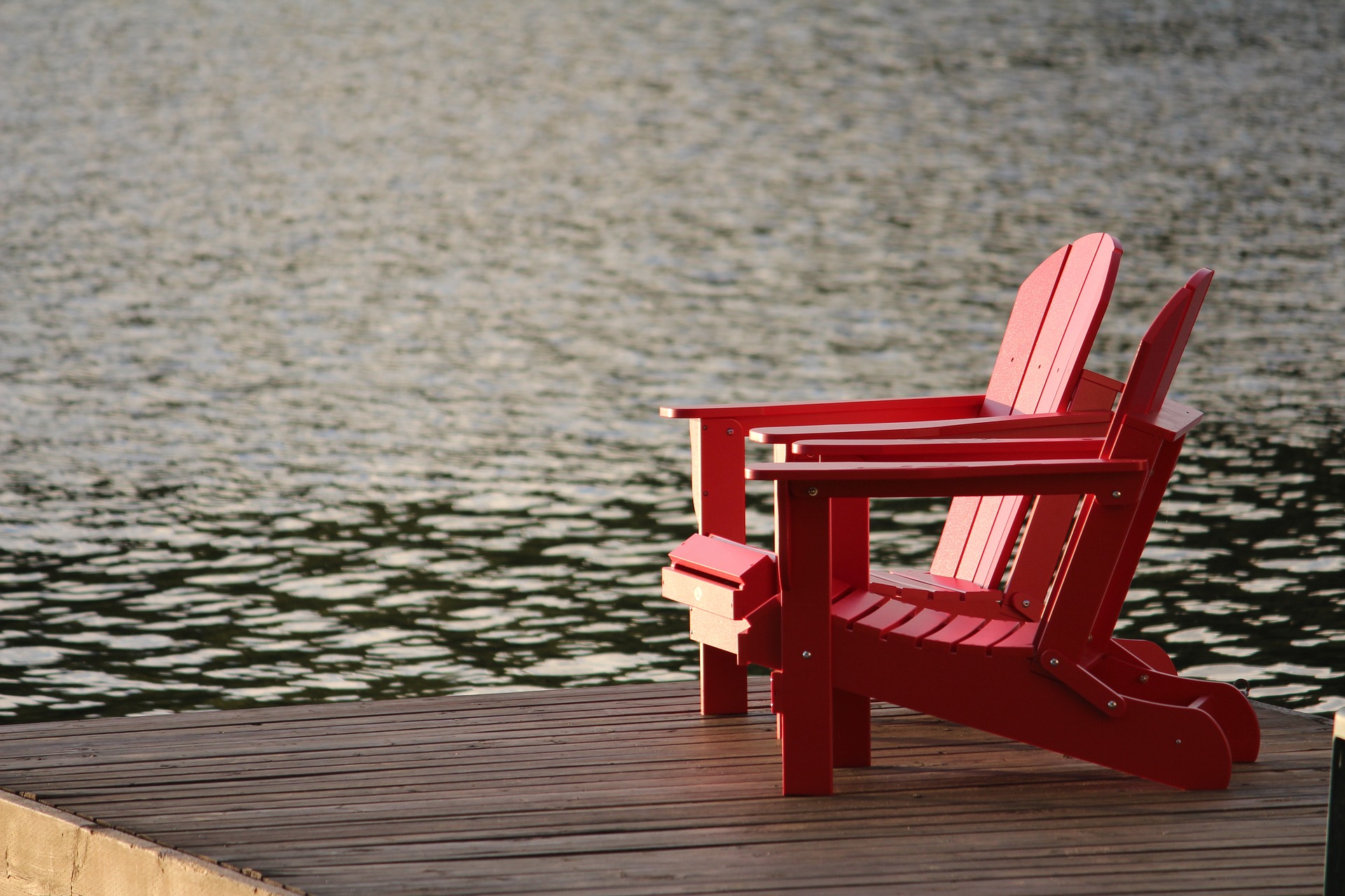Two red Muskoka chairs on a dock