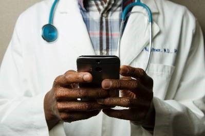 A mid-section view of a doctor in a lab coat looking at his smart phone. 