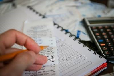 Close-up view of a person working on their taxes. Shown: hand, receipt, notebook, calculator.