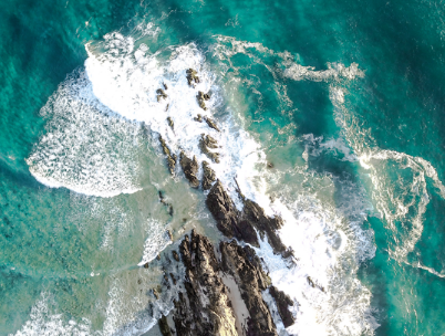Bird's eye view of waves crashing into rock in page