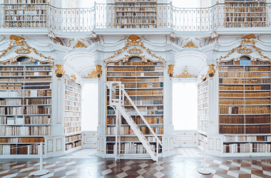 Ornate white library with full shelves and daylight streaming in.