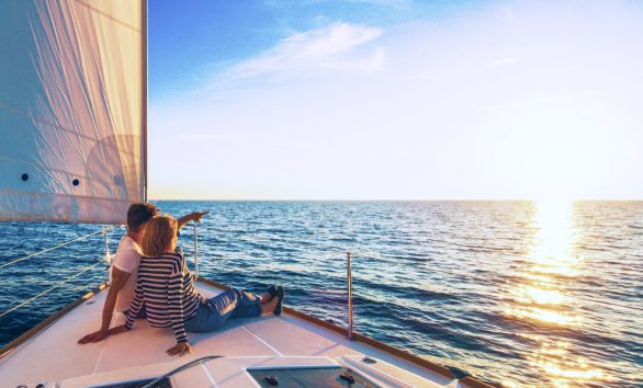 Two people looking out at the ocean from the bow of a sailboat.
