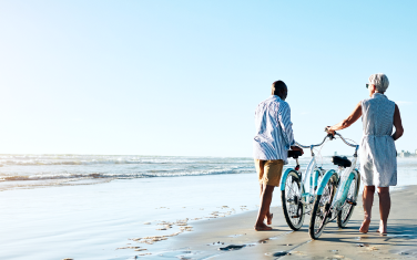 Two people pushing a bike on a beach.