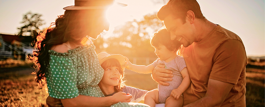 Parents hugging their two young children at golden hour.