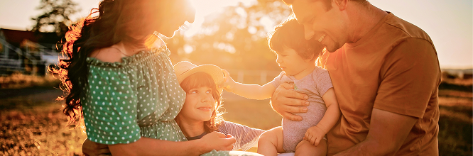 Parents hugging their two young children at golden hour.