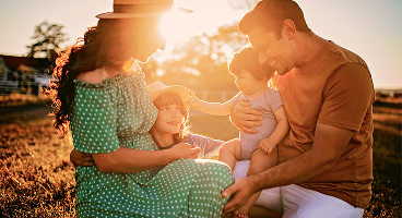 Parents hugging their two young children at golden hour.