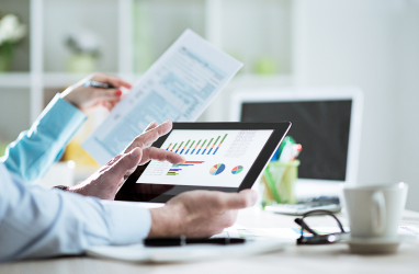 Two people looking at charts on a tablet and information in a printed document