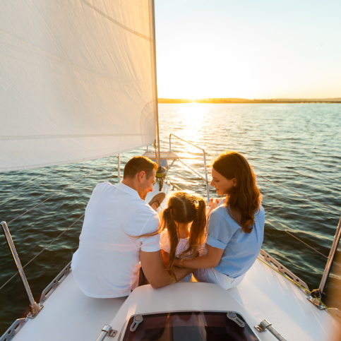 Parents and their child enjoying the sunset on a sailboat.