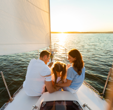 Parents and their child enjoying the sunset on a sailboat.