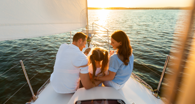 Parents and their child enjoying the sunset on a sailboat.