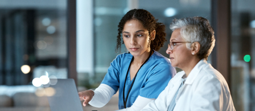 A person in scrubs and a person in a lab coat examining data.