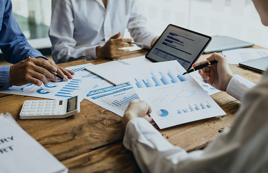 People analyzing graphs on paper and a computer on a table.