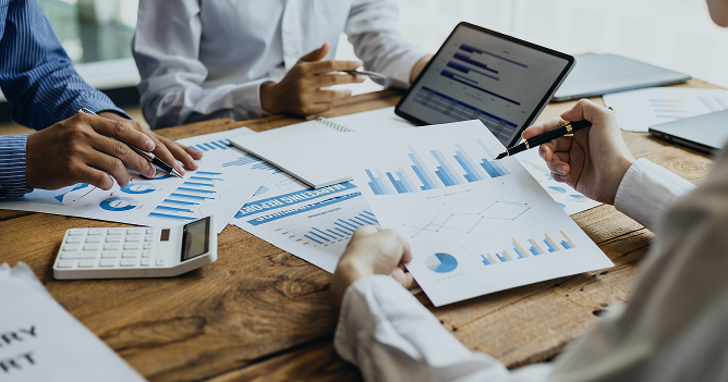 People analyzing graphs on paper and a computer on a table.