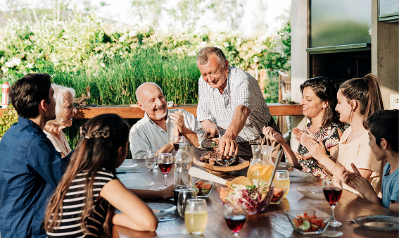 A multigenerational family around a table sharing a meal outdoors.