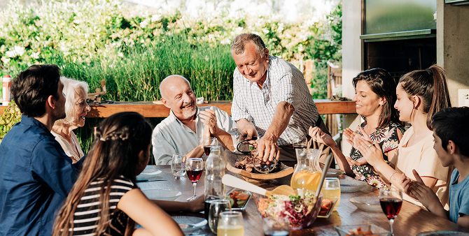 A multigenerational family around a table sharing a meal outdoors.