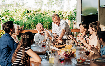 A multigenerational family around a table sharing a meal outdoors.