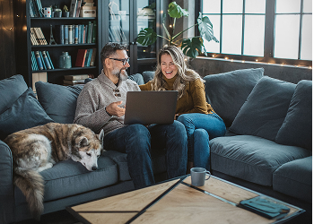 Two people and a dog looking at a laptop on a couch.