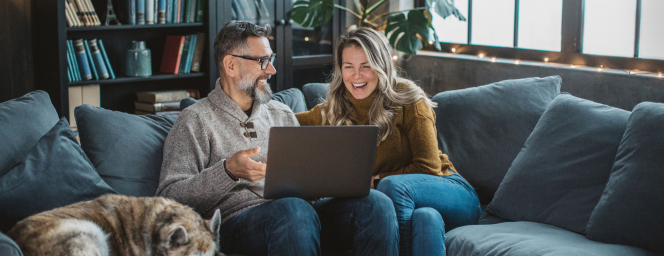 Two people and a dog looking at a laptop on a couch.