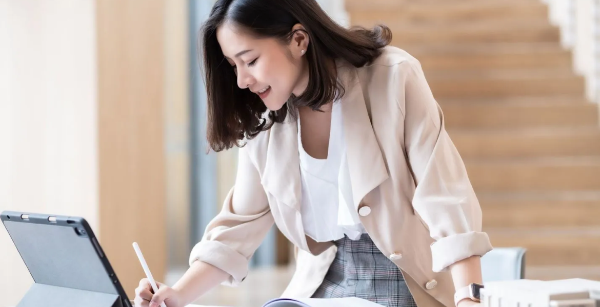 Business woman writing on some papers with a tablet on her desk