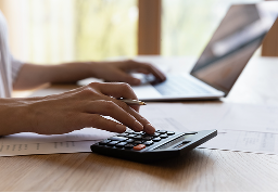 A close up of a wealth professional with their laptop open while using a calculator.